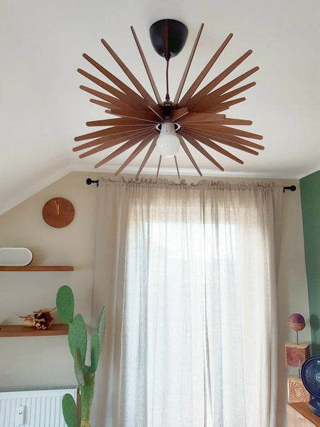 May include: A wooden ceiling fan with a starburst design. The fan has a white lightbulb and is hanging from a white ceiling.